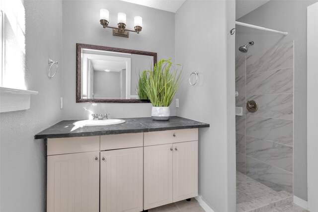 bathroom featuring tile patterned flooring, vanity, and a tile shower