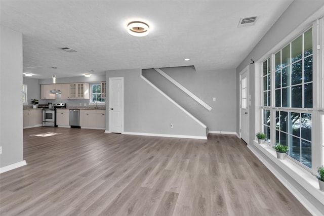 509 Spruce Dr, Conroe, TX 77302 - unfurnished living room with baseboards, light wood-style floors, stairs, a textured ceiling, and a sink