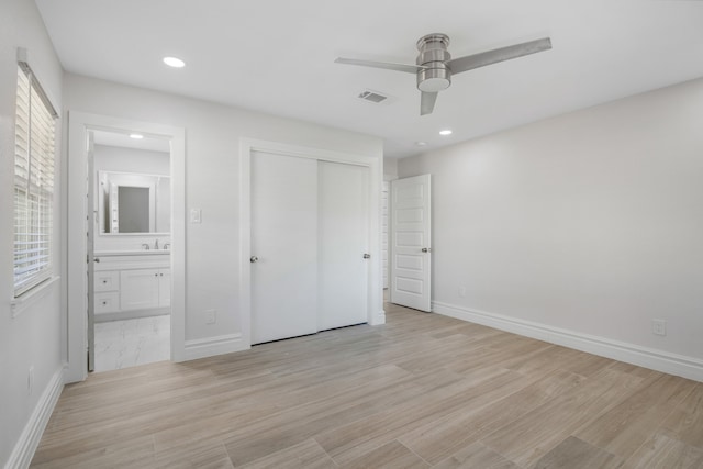 unfurnished bedroom with ensuite bath, ceiling fan, multiple windows, light hardwood / wood-style floors, and a closet