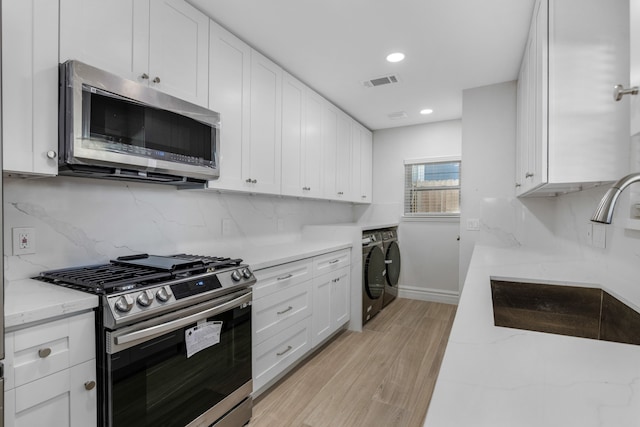 kitchen featuring sink, independent washer and dryer, light hardwood / wood-style floors, white cabinetry, and stainless steel appliances