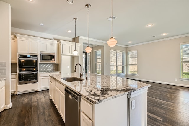 kitchen with hanging light fixtures, appliances with stainless steel finishes, a kitchen island with sink, and a healthy amount of sunlight