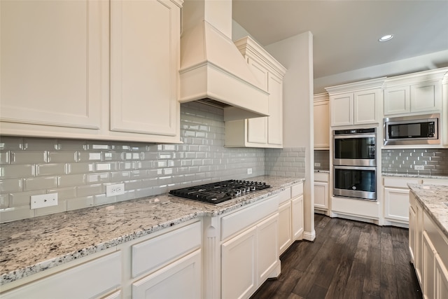 kitchen with decorative backsplash, appliances with stainless steel finishes, light stone countertops, premium range hood, and dark wood-type flooring