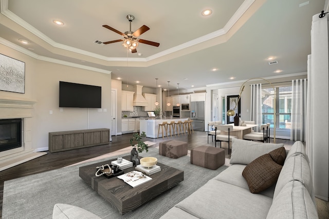 living room featuring wood-type flooring, a raised ceiling, ceiling fan, and ornamental molding