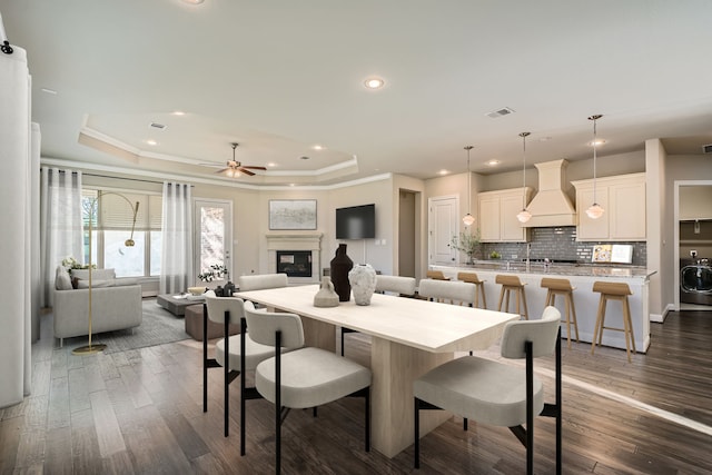 dining room featuring dark wood-type flooring, ceiling fan, ornamental molding, a tray ceiling, and washer / dryer