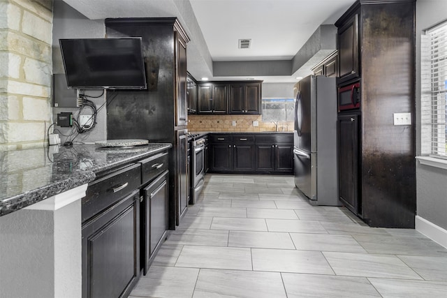 kitchen with dark brown cabinetry, stainless steel appliances, a healthy amount of sunlight, and dark stone countertops