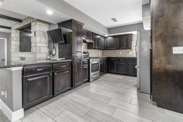 kitchen with dark stone countertops, decorative backsplash, dark brown cabinets, and appliances with stainless steel finishes