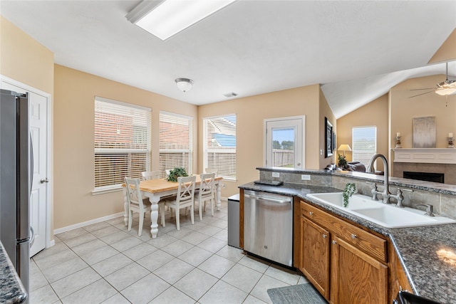 kitchen with brown cabinets, light tile patterned floors, appliances with stainless steel finishes, open floor plan, and a sink