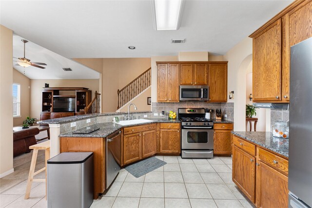 kitchen with sink, a breakfast bar area, dark stone countertops, appliances with stainless steel finishes, and kitchen peninsula