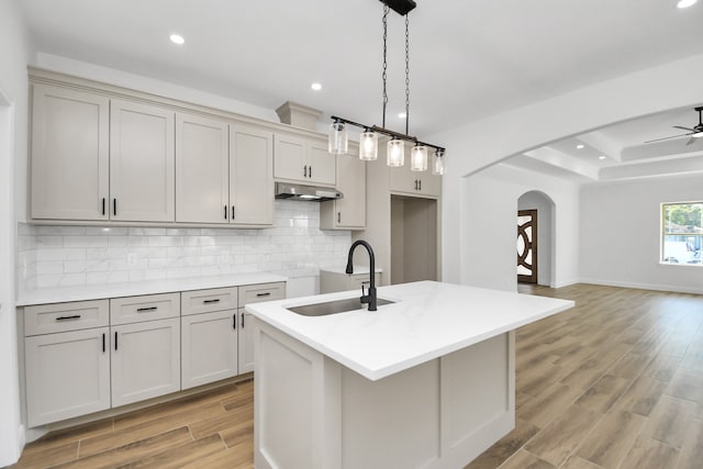 kitchen featuring light wood-type flooring, an island with sink, hanging light fixtures, and sink