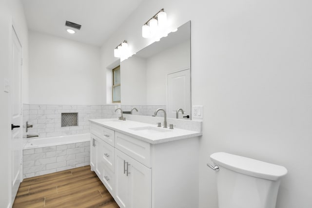 bathroom featuring vanity, a relaxing tiled tub, toilet, and wood-type flooring