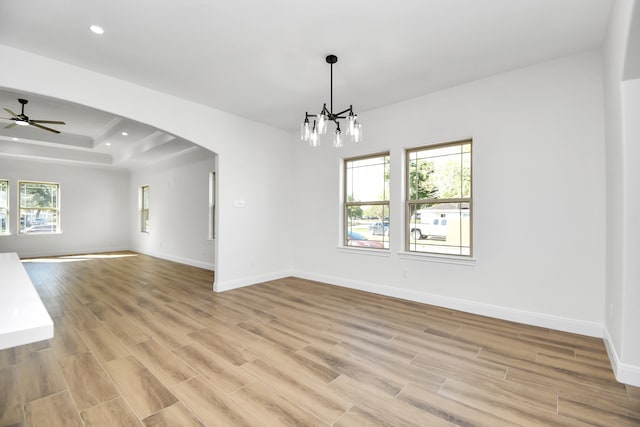 unfurnished room with ceiling fan with notable chandelier, light hardwood / wood-style floors, a raised ceiling, and a wealth of natural light