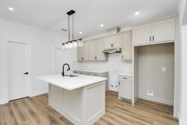 kitchen with tasteful backsplash, a kitchen island with sink, sink, light hardwood / wood-style flooring, and hanging light fixtures