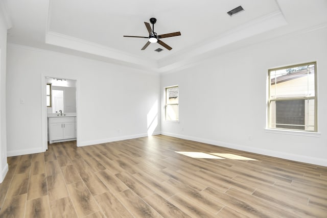 interior space with ceiling fan, light wood-type flooring, connected bathroom, and a tray ceiling