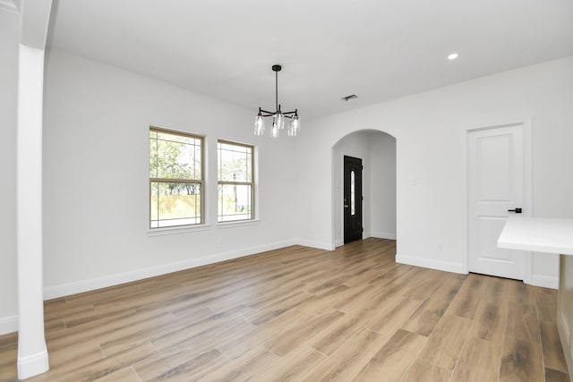 empty room featuring a chandelier and light hardwood / wood-style floors