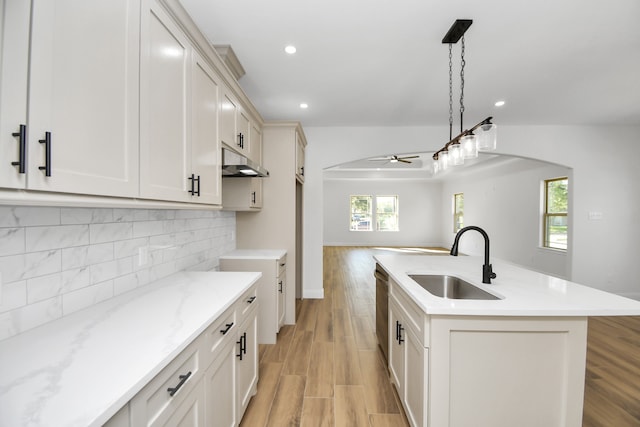 kitchen with ceiling fan, sink, decorative light fixtures, light hardwood / wood-style flooring, and an island with sink