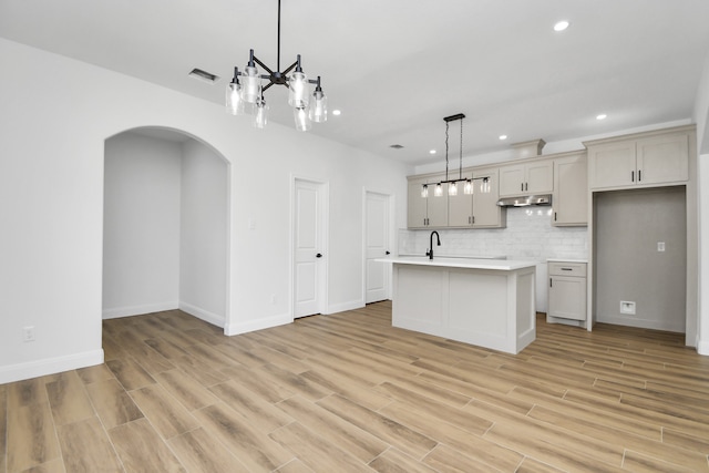 kitchen featuring pendant lighting, an inviting chandelier, a center island with sink, light hardwood / wood-style flooring, and gray cabinets