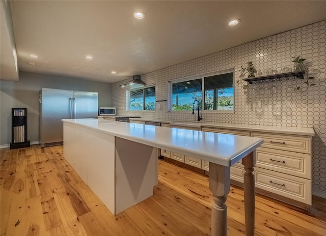 kitchen featuring a center island, wall chimney range hood, sink, light hardwood / wood-style flooring, and stainless steel refrigerator