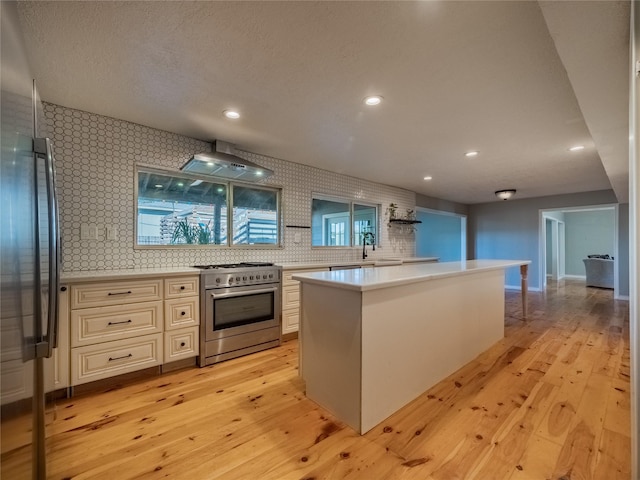 kitchen with wall chimney range hood, high end stainless steel range oven, a wealth of natural light, tasteful backsplash, and light hardwood / wood-style floors