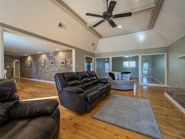 living room featuring lofted ceiling with beams, light hardwood / wood-style floors, ceiling fan, and brick wall