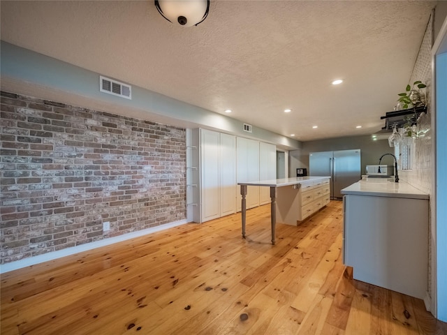 kitchen featuring stainless steel fridge, light wood-type flooring, a textured ceiling, a breakfast bar area, and brick wall