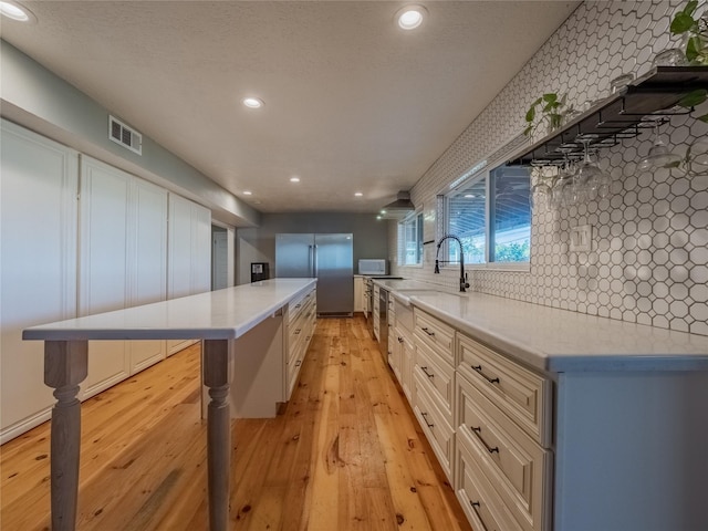 kitchen with light wood-type flooring, backsplash, sink, stainless steel refrigerator, and a large island