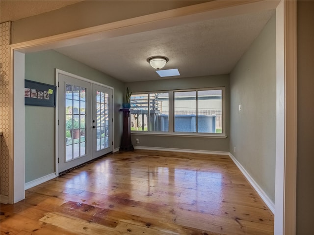 doorway with french doors, a healthy amount of sunlight, a textured ceiling, and light hardwood / wood-style floors