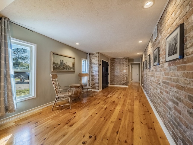 hall with light hardwood / wood-style flooring, brick wall, and a textured ceiling