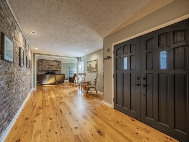 foyer featuring a textured ceiling, light hardwood / wood-style flooring, and brick wall