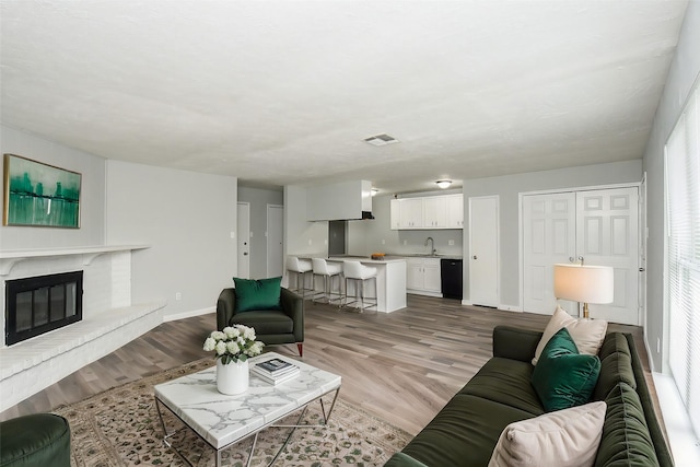 living room featuring a brick fireplace, sink, and light hardwood / wood-style floors