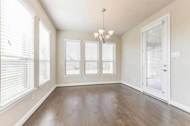 unfurnished dining area featuring plenty of natural light, dark wood-type flooring, and an inviting chandelier