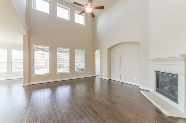 unfurnished living room featuring dark hardwood / wood-style flooring, a towering ceiling, ceiling fan, and a healthy amount of sunlight