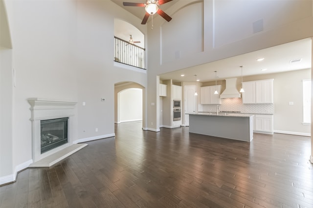 unfurnished living room with ceiling fan, sink, dark wood-type flooring, and a high ceiling