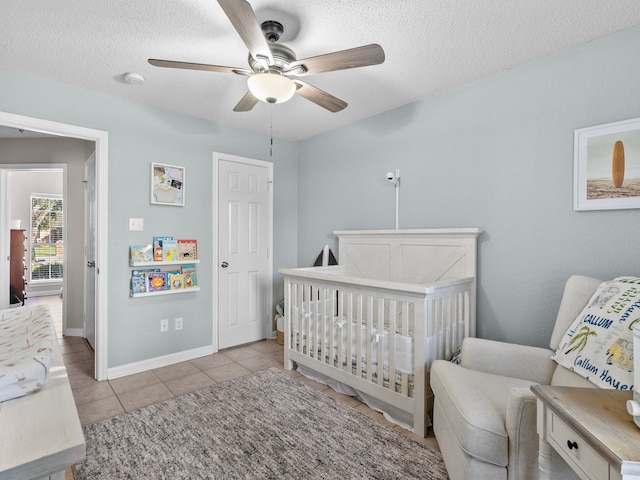 bedroom with ceiling fan, light tile patterned floors, a textured ceiling, and a nursery area