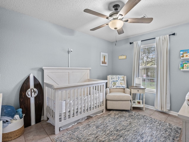 tiled bedroom with ceiling fan, a nursery area, and a textured ceiling