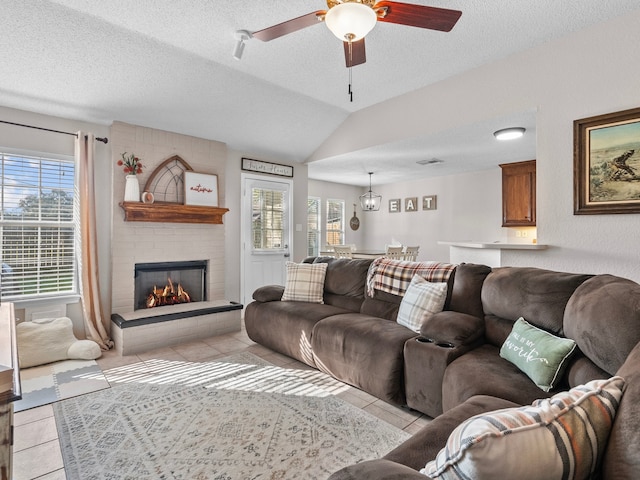 tiled living room with a textured ceiling, ceiling fan, a large fireplace, and lofted ceiling