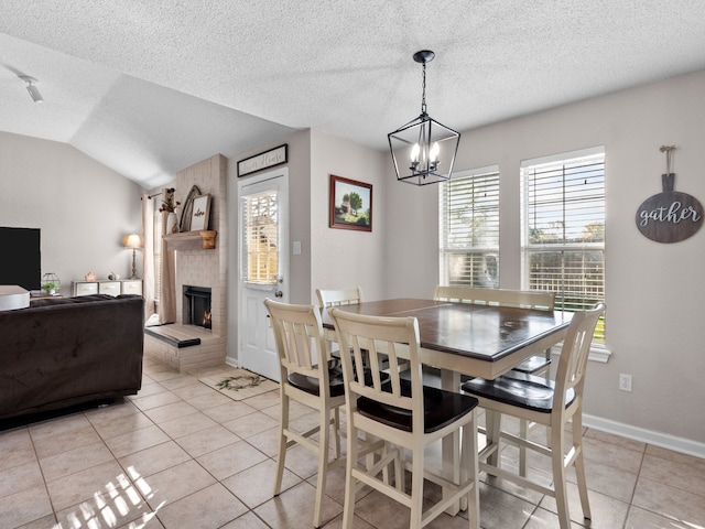 tiled dining room with a textured ceiling, a fireplace, a chandelier, and vaulted ceiling