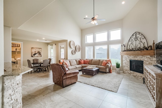 living room featuring ceiling fan, washing machine and dryer, a stone fireplace, a towering ceiling, and light tile patterned floors