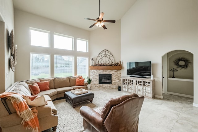 living room featuring a towering ceiling, a stone fireplace, and ceiling fan