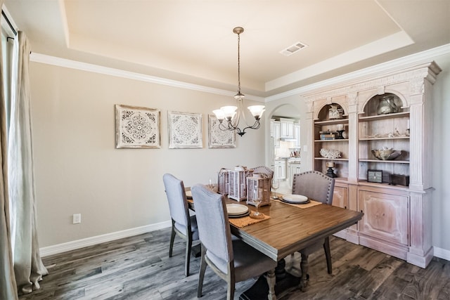 dining area with dark hardwood / wood-style flooring, an inviting chandelier, a raised ceiling, and ornamental molding