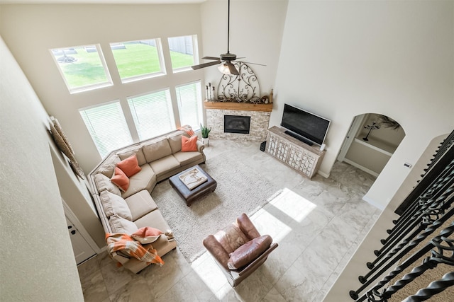 living room with ceiling fan, a stone fireplace, and high vaulted ceiling