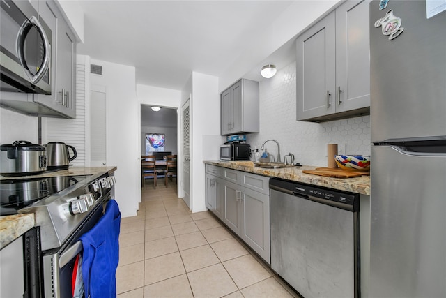 kitchen featuring light stone countertops, sink, light tile patterned floors, and stainless steel appliances