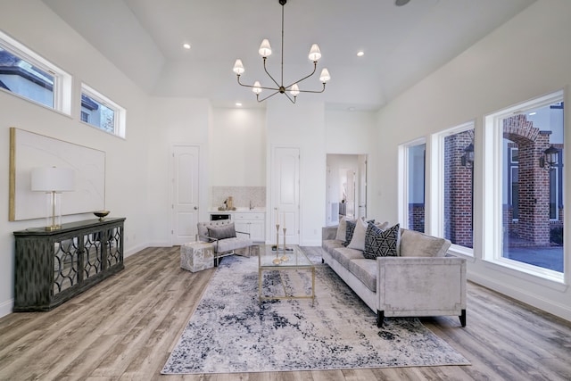 living room featuring a towering ceiling, a healthy amount of sunlight, a notable chandelier, and light hardwood / wood-style floors