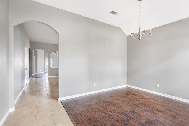 spare room with a chandelier, lofted ceiling, and light hardwood / wood-style flooring