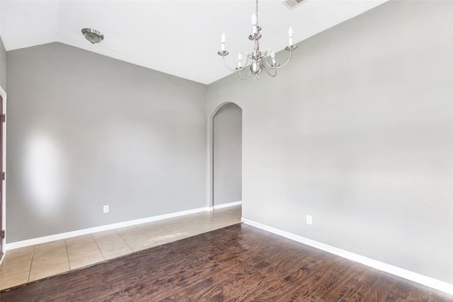 empty room with hardwood / wood-style flooring, an inviting chandelier, and vaulted ceiling