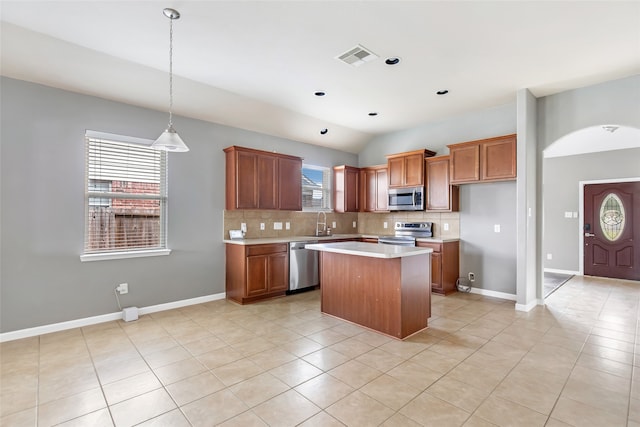 kitchen with appliances with stainless steel finishes, a center island, light tile patterned floors, and lofted ceiling