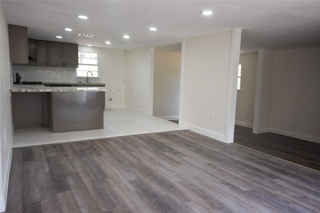 kitchen featuring hardwood / wood-style floors, decorative backsplash, light stone counters, and sink