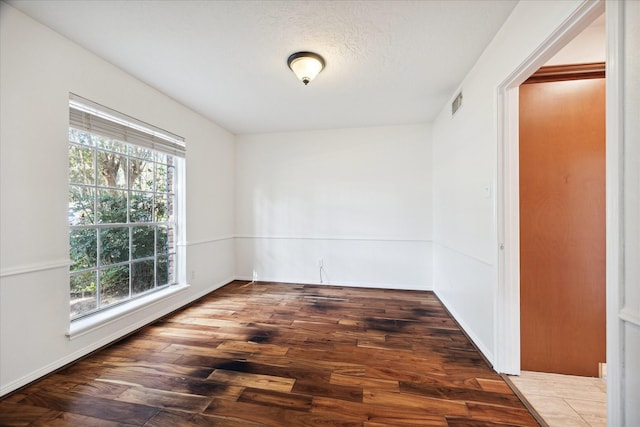 empty room featuring a textured ceiling, wood finished floors, visible vents, and baseboards