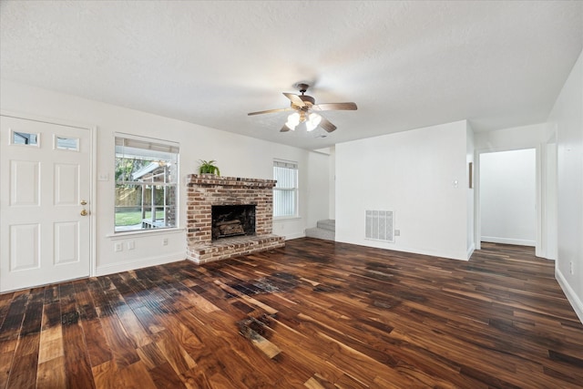 unfurnished living room with ceiling fan, a textured ceiling, wood finished floors, visible vents, and a brick fireplace