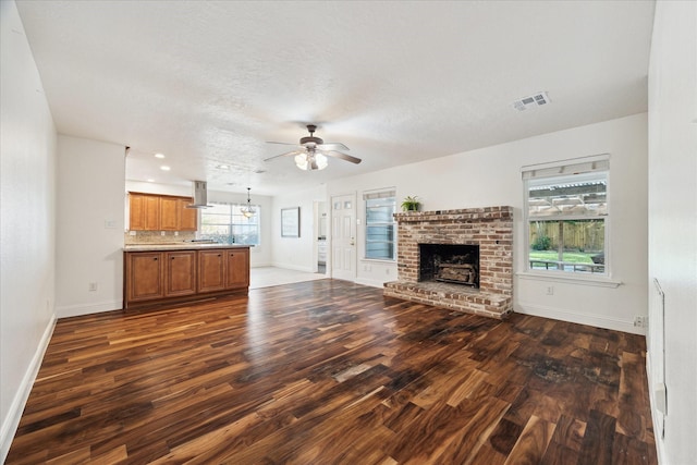 unfurnished living room with ceiling fan, a fireplace, visible vents, baseboards, and dark wood-style floors