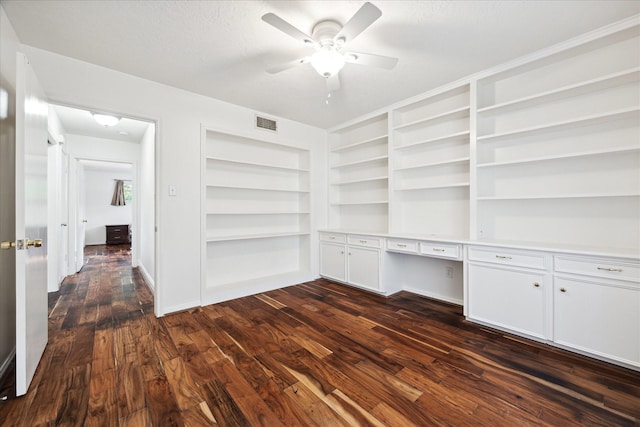 unfurnished office featuring ceiling fan, a textured ceiling, dark wood-type flooring, visible vents, and built in desk